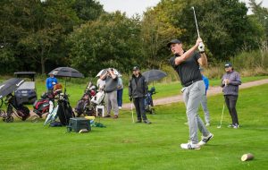 man hitting a golf ball on golf course wearing black t shirt and hat