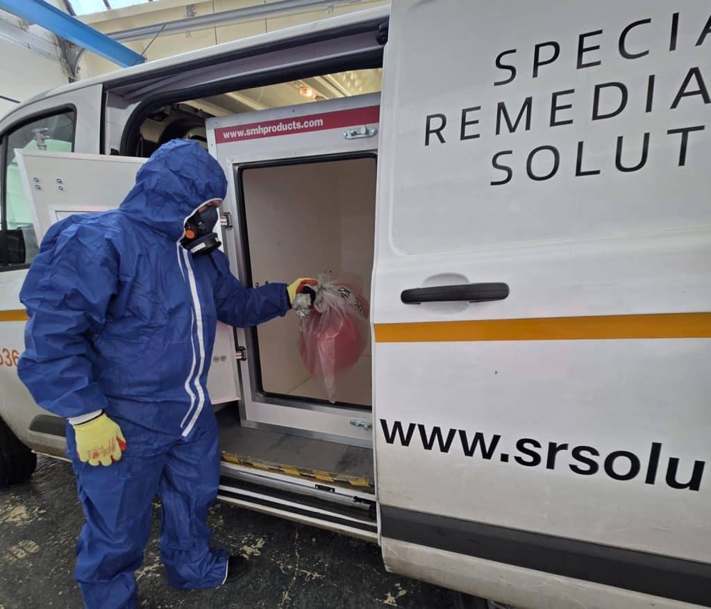 man in blue hazard suit with mask on standing next to van