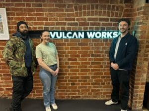 two men and one lady, young, looking into camera next to sign saying vulcan works